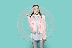 Excited positive teenager girl pointing index finger away, showing copy space for advertisement.