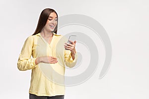 Excited Pregnant Girl Holding Phone Standing On White Studio Background