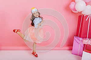 Excited pretty birthday girl with long brunette hair, in tulle skirt jumping, having fun isolated on pink background
