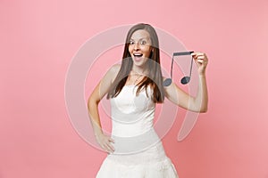 Excited pretty bride woman in white wedding dress holding musical note choosing staff, musicians or DJ isolated on