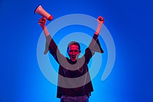 Excited pretty girl, student and agitator with short hair in black sweater shouting at megaphone isolated on blue