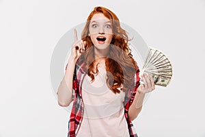 Excited pretty young redhead lady holding money have an idea.