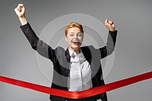 excited redhead businesswoman crossing finish ribbon
