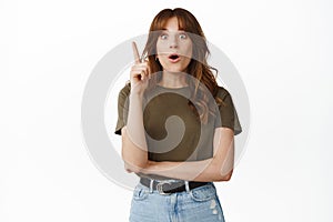 Excited redhead girl raise finger, have suggestion, pitching an idea, great plan, gasping amazed, standing against white