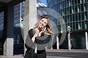 Excited saleswoman receive good news on phone and rejoicing, walking on street and celebrating, making fist pump while