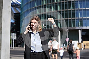 Excited saleswoman receive good news on phone and rejoicing, walking on street and celebrating, making fist pump while