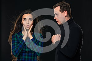 Excited scared nervous woman look into camera, man stand by side, have eyes full in disbelief. On black background