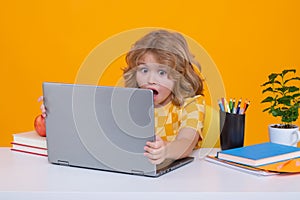 Excited school child using laptop computer. Back to school. Portrait of cute child school boy, isolated on yellow studio