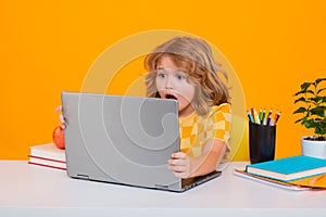 Excited school child using laptop computer. School child portrait isolated on yellow studio background. Kid boy from