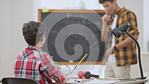 Excited schoolboy gesturing and talking in slow motion discussing matter with teacher in classroom. Back view of