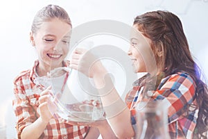 Excited schoolgirls grinning widely while holding flask in school lab