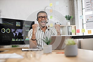 Excited screaming young african american business man or entrepreneur working with laptop