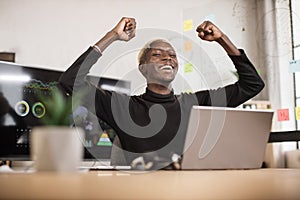 Excited screaming young african business man or entrepreneur working with laptop computer