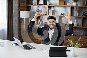 Excited screaming young business man triumphing with raised hands because successful business deal.