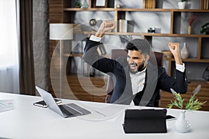 Excited screaming young business man triumphing with raised hands because successful business deal.