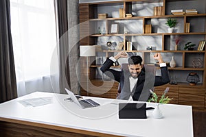 Excited screaming young business man triumphing with raised hands because successful business deal.