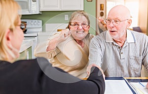 Excited Senior Adult Couple Celebrating Over Documents in Their Home with Agent At Signing