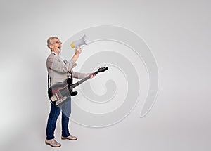 Excited senior businesswoman shouting over megaphone and playing electric guitar on white background