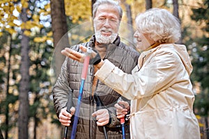 Excited senior couple standing with nordic walking poles in colorful autumn park.