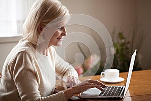 Excited senior lady browsing web using laptop at home