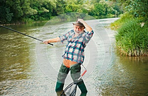 Excited senior man fisherman with fishing rod, spinning reel on river. Old man catching fish, pulling rod while fishing