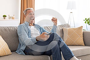 Excited senior man watching tv celebrating goal holding remote control