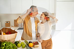 Excited senior spouses unpacking bag, arriving from supermarket, standing in kitchen and having fun together