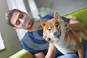 Excited Shiba Inu dog sitting on green sofa with best friend, young caucasian man