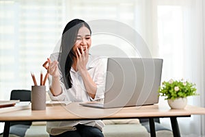 Excited, shocked and cheerful Asian businesswoman looking at her laptop screen