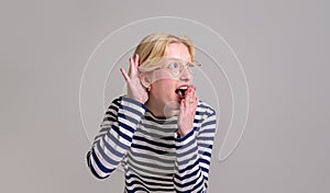 Excited shocked young woman covering her mouth with hand while listening gossip on white background