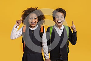 Excited siblings with school backpacks on yellow background