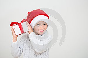 Excited smiling little boy in red santa hat with gift box isolated on white background, banner copy space. Christmas