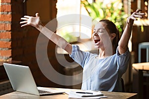 Excited smiling woman celebrating online win, using laptop in cafe