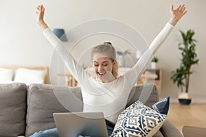 Excited smiling woman celebrating online win, using laptop at home