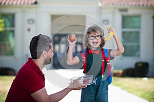 Excited son schoolboy eating tasty lunch outdoors. Happy father and son go to elementary school. Parent taking child to