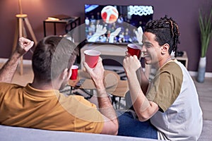 Excited sports fans watching match on TV at home and drinking beer