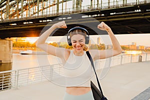 Excited sports woman gesturing while standing on embankment with bridge on background