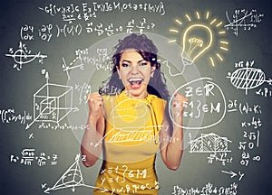 Excited student with idea light bulb and maths and science formulas on blackboard