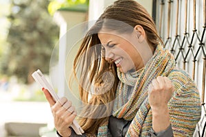 Excited student reading good news on line on a tablet computer in the street on a summer day