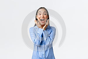 Excited super happy asian girl in blue pajamas waking up to awesome surprise, screaming from happiness looking at camera