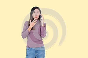 An excited and surprised Asian woman is talking on the phone, isolated yellow background