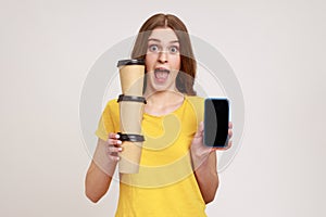Excited surprised female of young age in yellow casual T-shirt holding blank screen smartphone and