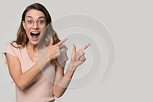 Excited surprised young woman wearing glasses pointing at copy space