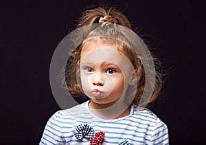 Excited surprising small kid girl looking fun with big eyes and grimacing face and pouted lips on black studio background. Closeup