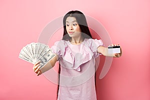 Excited teen asian girl stretch out hands with dollar bills and plastic credit card, look at money with amazement
