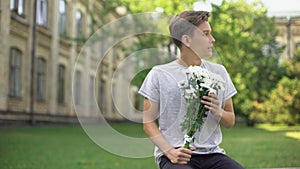 Excited teen boy with bouquet of flowers waiting for girlfriend, anticipation