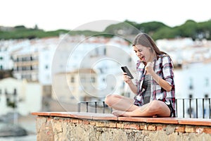 Excited teenage girl reading online phone content on a ledge