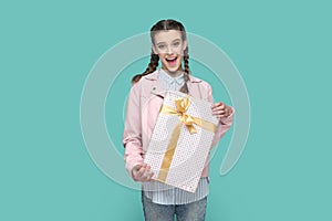 Excited teenager girl holds present box in hands, looking at camera, waiting holiday to give gift