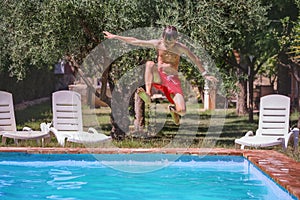 Excited teenager in jumping action into a serene summer pool