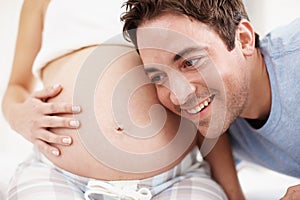 Excited to become a father. An excited man listening to his child moving in his wifes stomach.